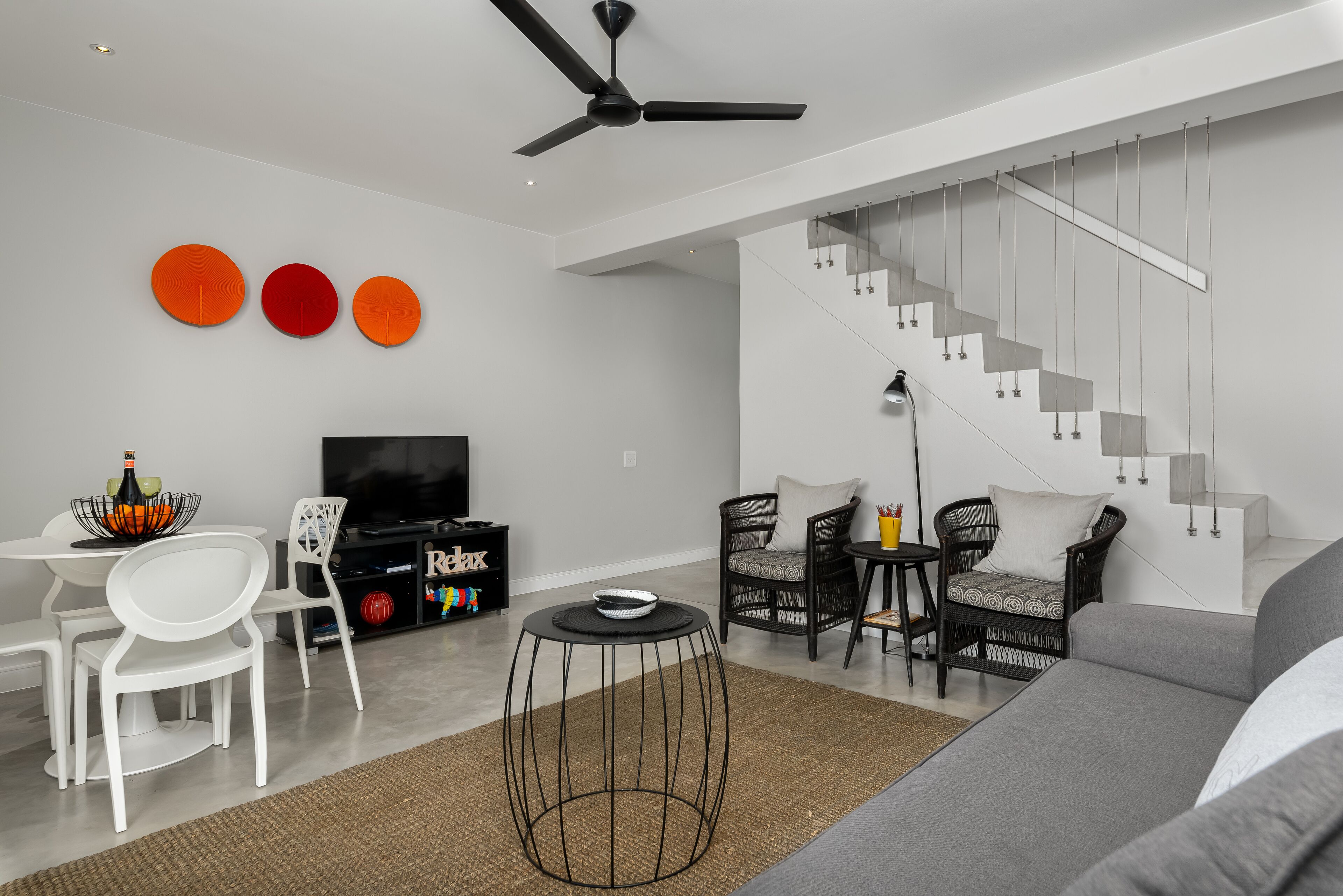 A modern living room with a staircase, white furniture, and a TV.