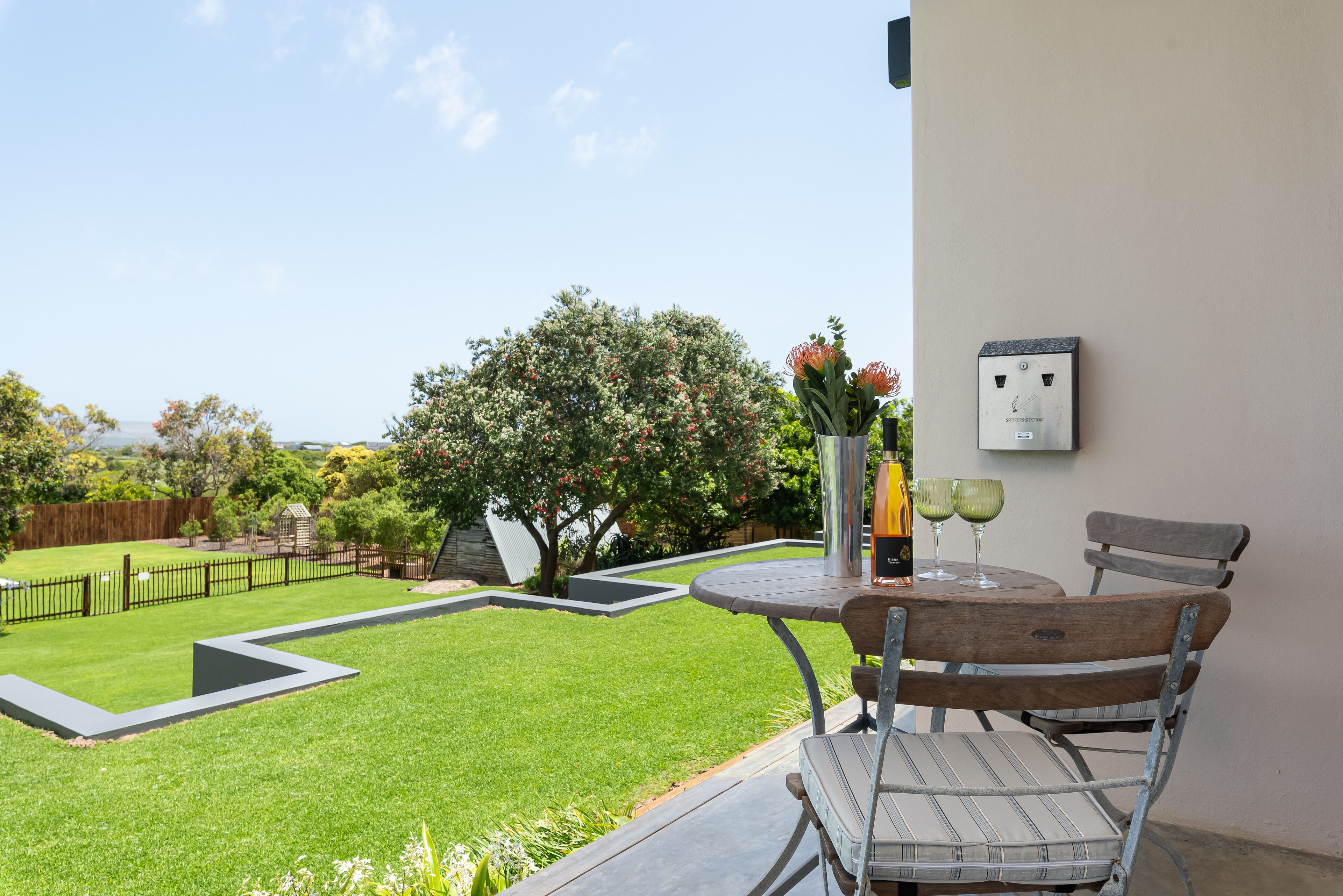 A patio with a table and chairs, a small garden, and a power outlet on the wall.