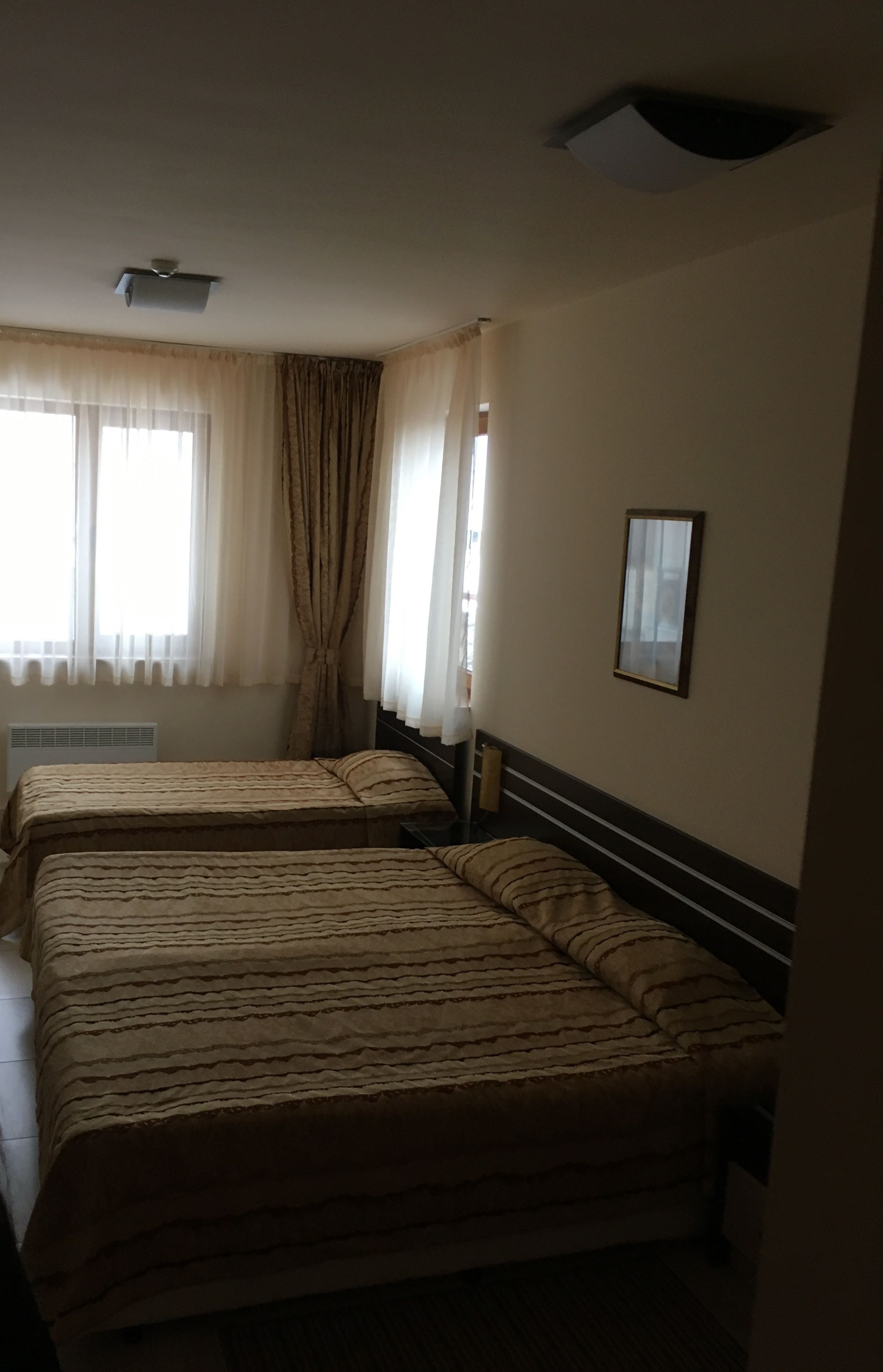 A hotel room with two beds, a ceiling fan, a window with curtains, and a framed picture on the wall.