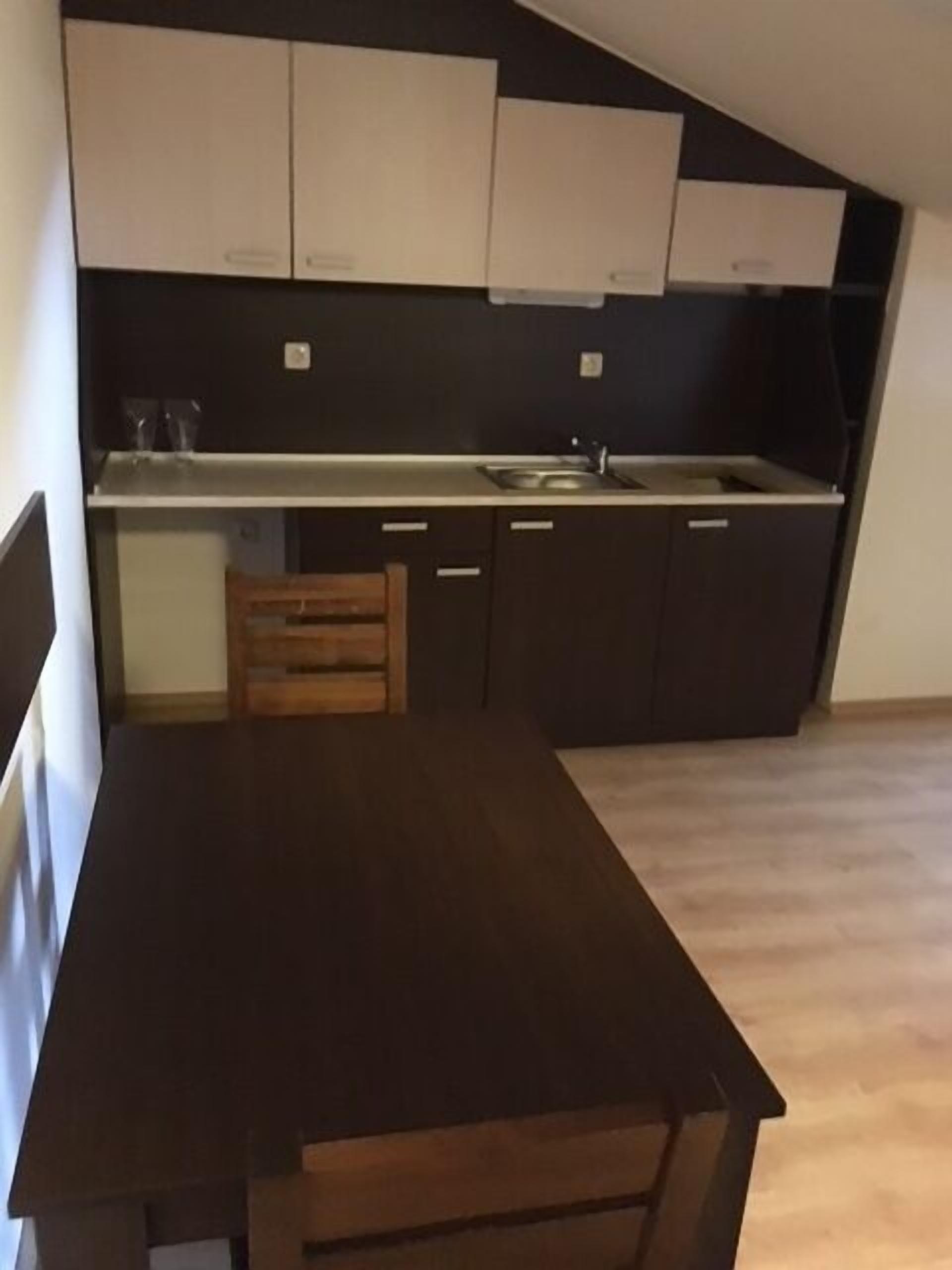 Une cuisine avec des meubles de couleur sombre, une table en bois et un plan de travail de couleur claire.