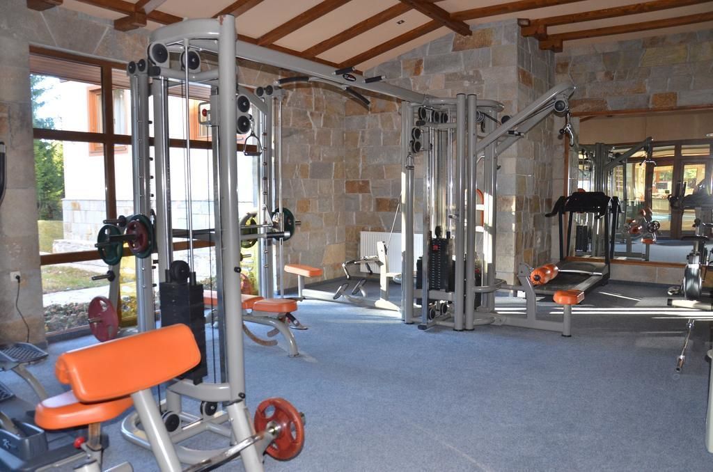 Une salle de sport équipée de divers appareils d’exercice, avec des murs en pierre et de grandes fenêtres.