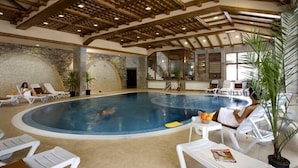 En indendørs swimmingpool med liggestole og plantekasser.