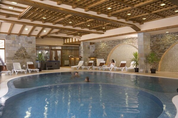 An indoor swimming pool with lounge chairs and stone walls.