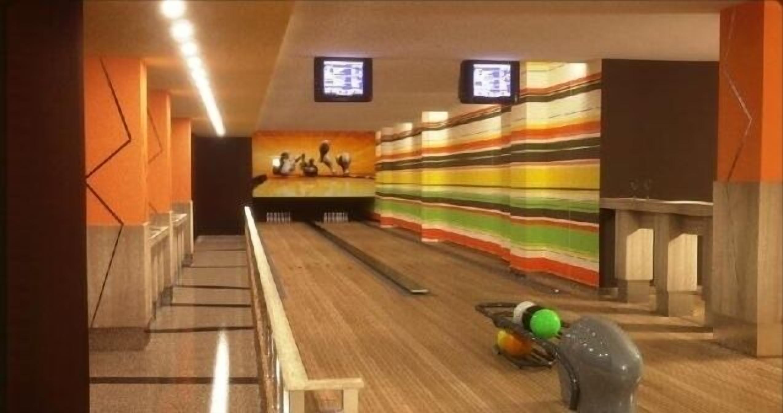 A bowling alley with wooden lanes, a colorful striped wall, and two televisions mounted on the ceiling.