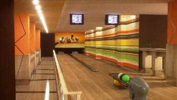 A bowling alley with wooden lanes, a colorful striped wall, and two televisions mounted on the ceiling.