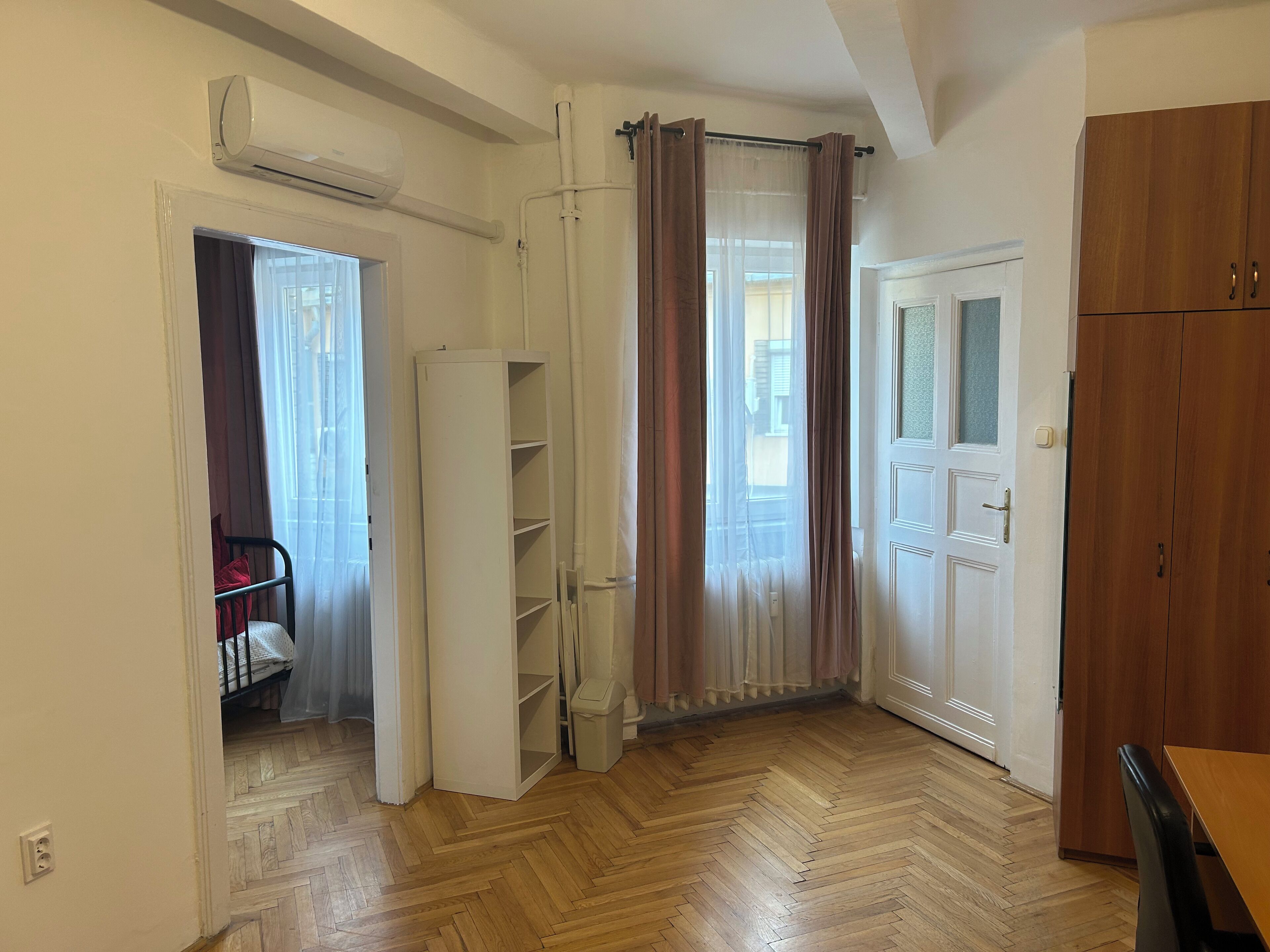 Una stanza con pavimento in parquet a spina di pesce, un'armadio bianco, una porta con pannello in vetro e un'intera parete con mensole bianche.