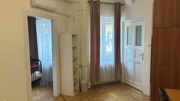 Una stanza con pavimento in parquet a spina di pesce, un'armadio bianco, una porta con pannello in vetro e un'intera parete con mensole bianche.