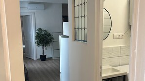 Un couloir avec une plante en pot, un réfrigérateur blanc et un revêtement mural en carreaux dans la zone cuisine.