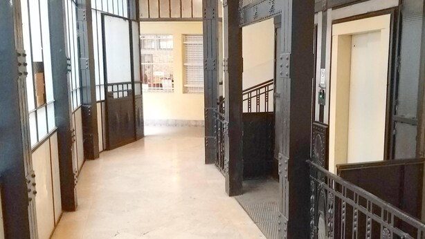 Un couloir doté d’un sol carrelé, de rampes en métal et d’un escalier muni d’une main courante.