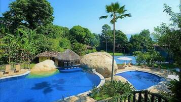 A pool area with two separate pools, a thatched-roof structure, and surrounding greenery.