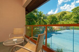Varanda com cadeiras de vime e uma mesa, com vista para uma piscina e vegetação exuberante.