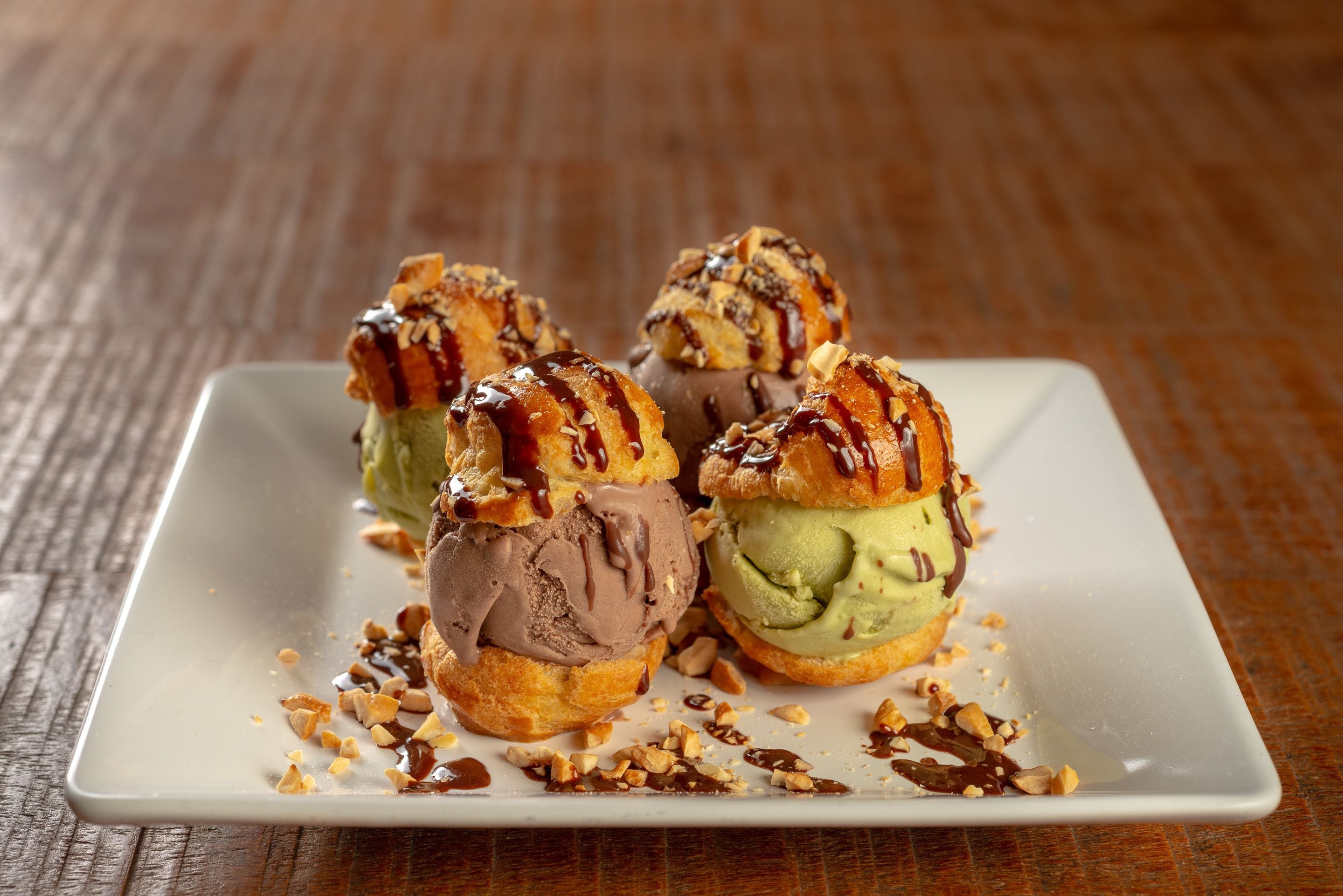 A square plate with four ice cream cones on a wooden table.