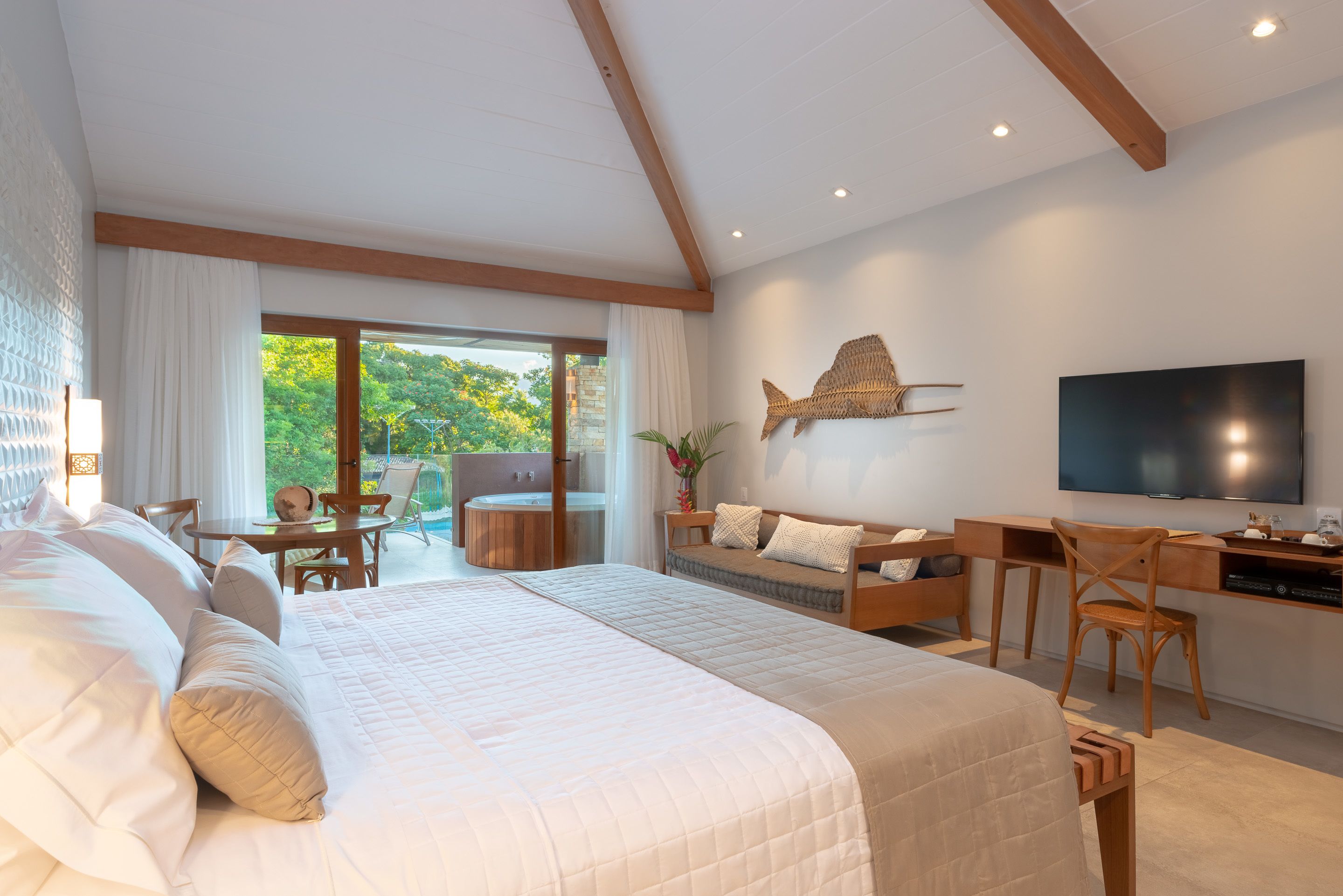 A modern hotel room with a large bed, a desk, a TV, and a view of the outdoors.