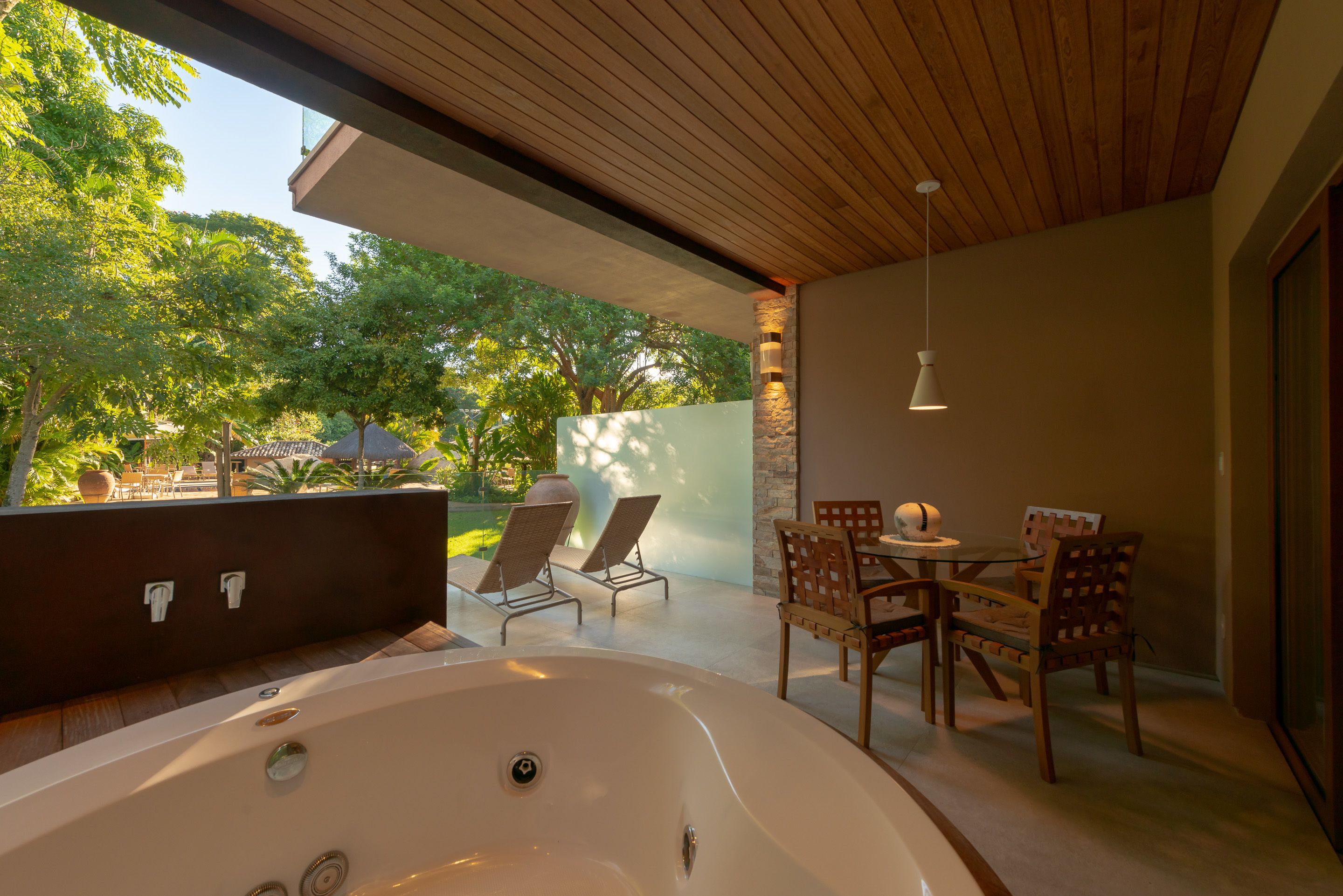 Een modern terras buiten met een jacuzzi, lounge fauteuils en een eethoek met houten meubels.