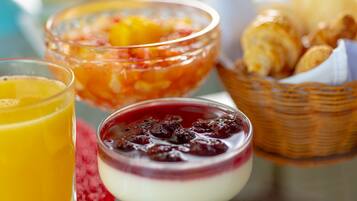 Una mesa de desayuno con un vaso de jugo de naranja, un bol de ensalada de frutas, un postre con bayas y una cesta de croissants.