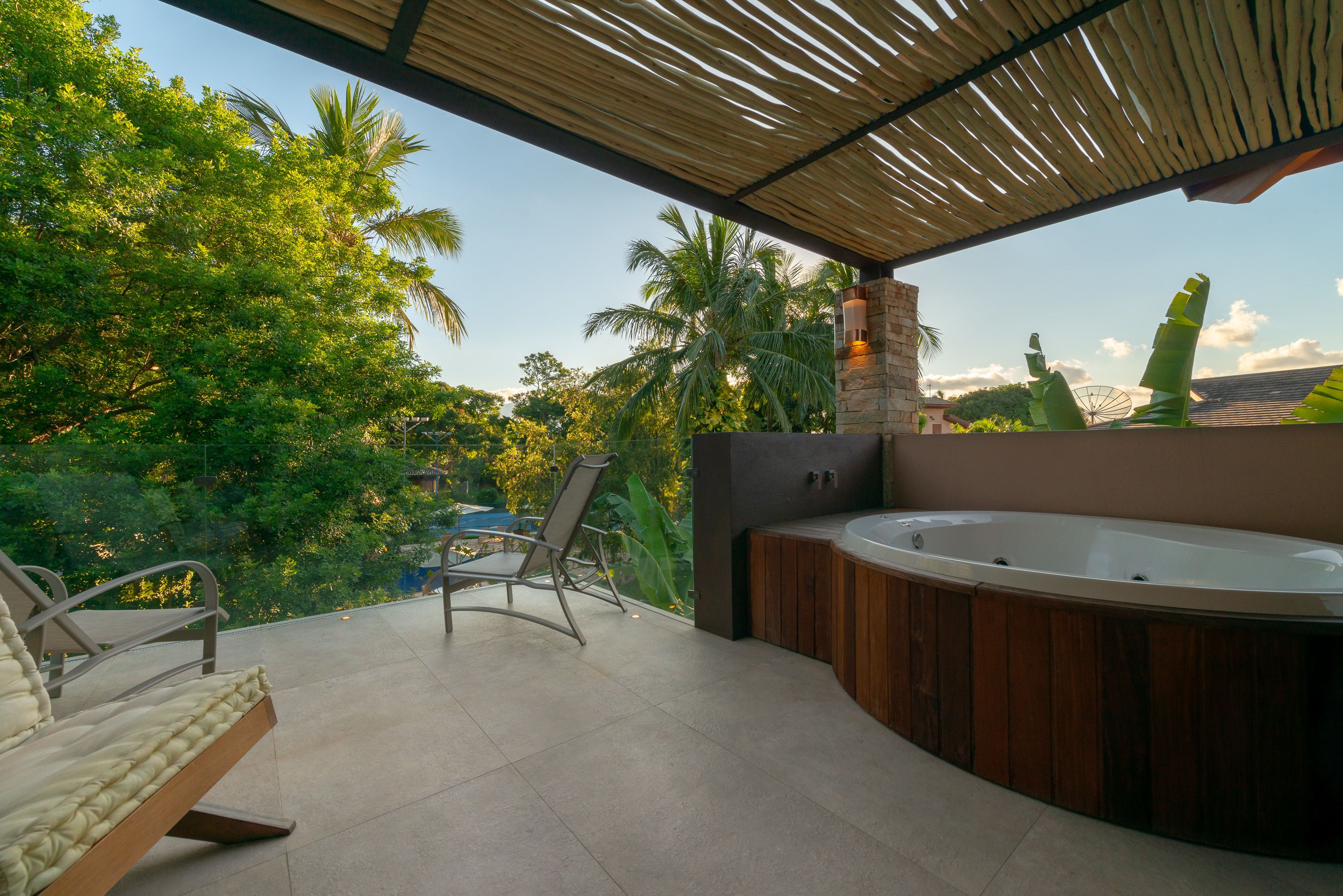 Een terras buiten met een jacuzzi, een zithoek en uitzicht op weelderige begroeiing.