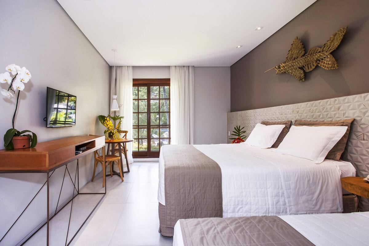 Una habitació d'hotel moderna amb un llit gran, un escriptori amb una cadira, una televisió i una finestra amb cortines.