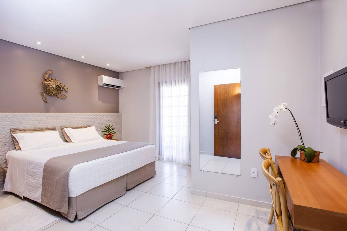 Una habitació d'hotel moderna amb un llit gran, un escriptori de fusta, una televisió i una finestra amb cortines.