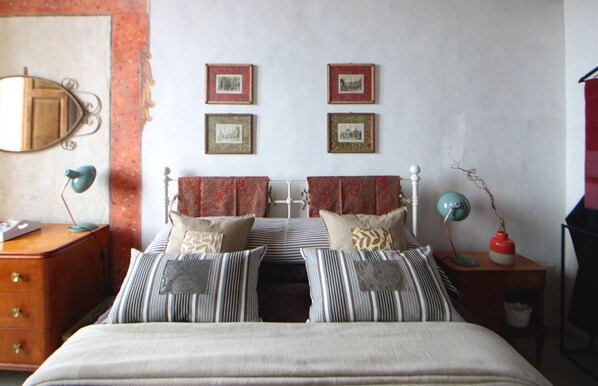 A bedroom with a bed, two bedside tables, a dresser, and a mirror. There are four framed pictures on the wall above the bed.