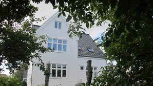 A two-story white house with a sloped roof, surrounded by a well-maintained lawn and trees. - Guesthouse Sharon Aarhus (Aarhus)