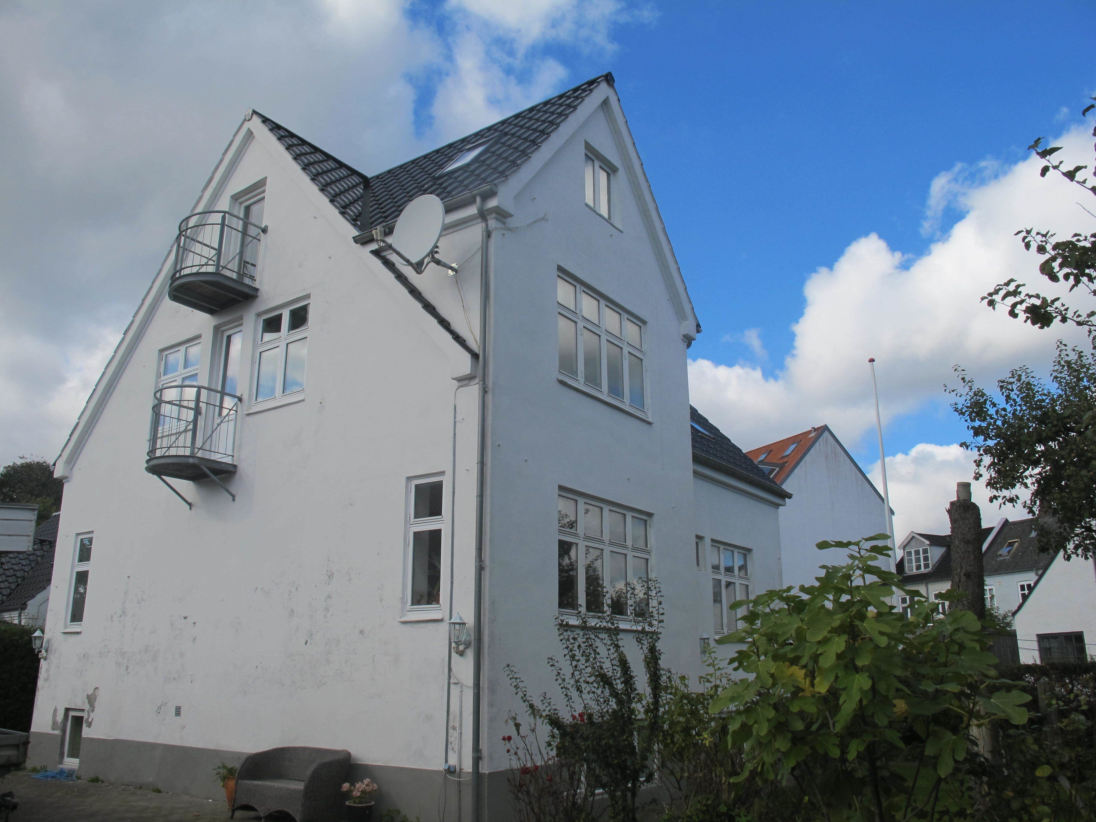A two-story white building with a satellite dish, a small balcony, and a red-tiled roof.