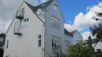 A two-story white building with a satellite dish, a small balcony, and a red-tiled roof.
