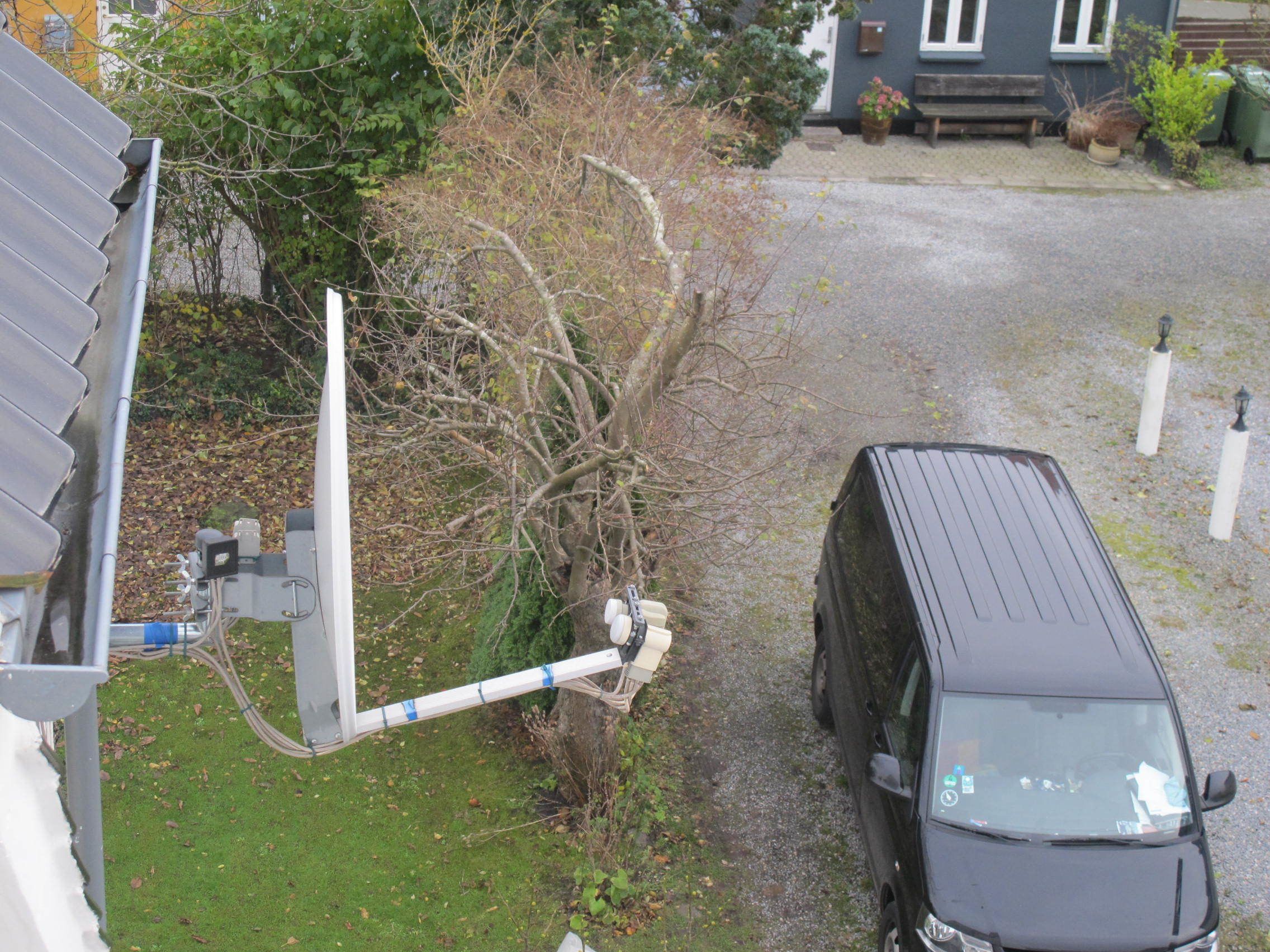A black SUV parked on a gravel driveway next to a house with a satellite dish.
