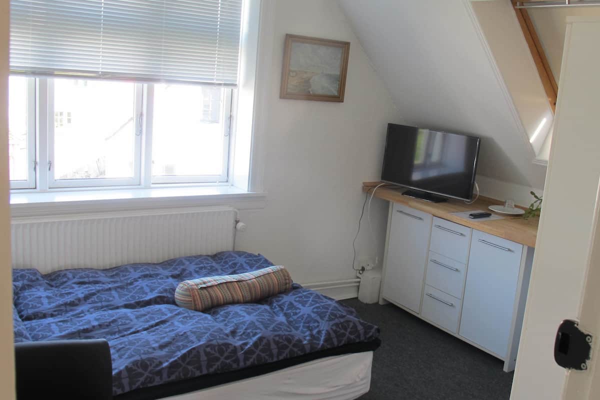 Ein Schlafzimmer mit einem Bett, einem Fernseher auf einem Schreibtisch und einem Fenster mit Jalousien.