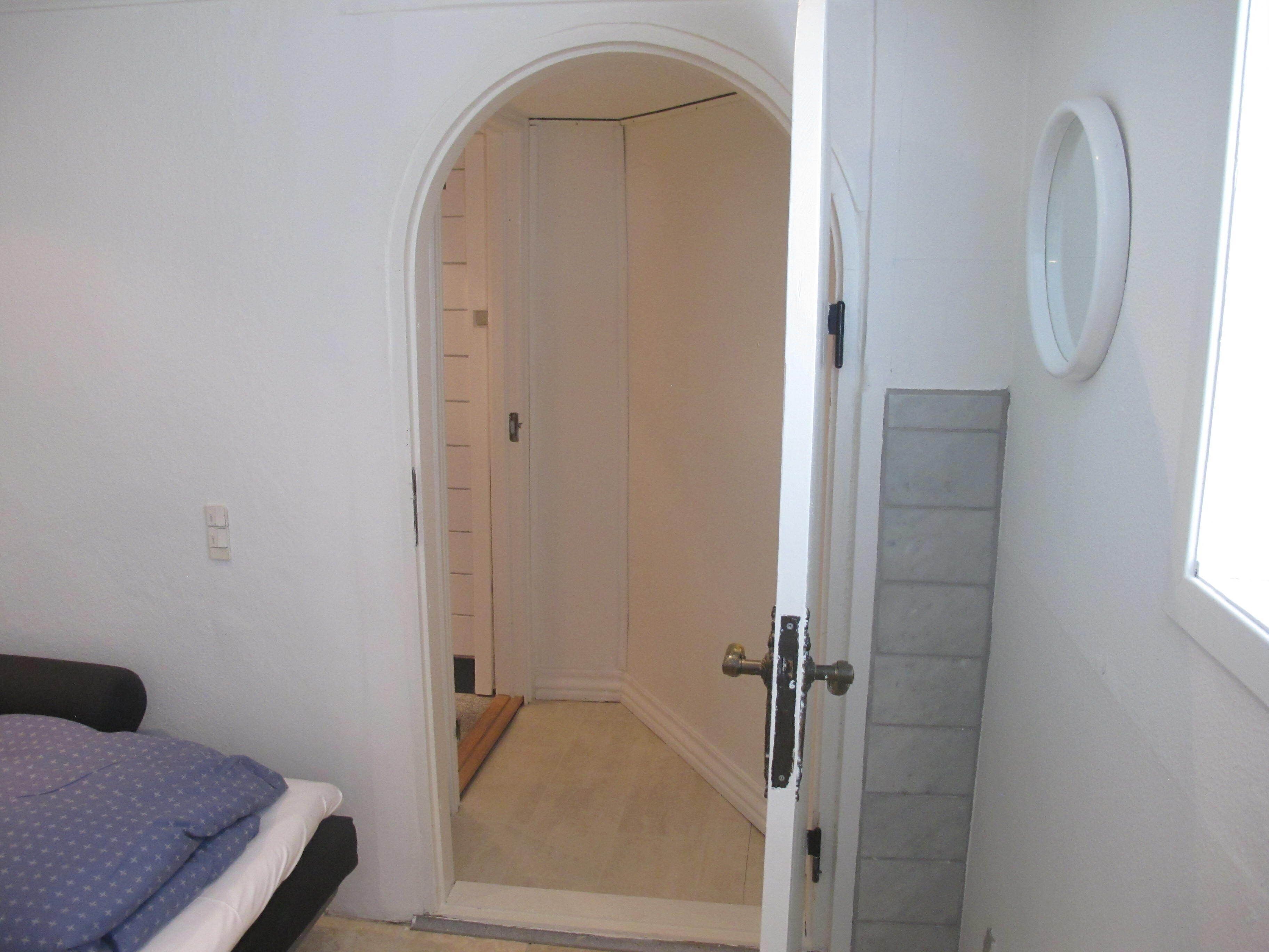 A bedroom with a bed, a door leading to a hallway, and a small window.