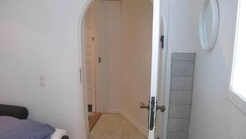 A bedroom with a bed, a door leading to a hallway, and a small window.