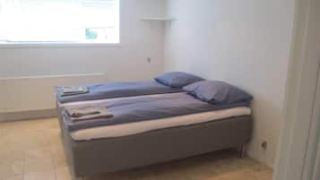 Una piccola camera singola con un letto, una finestra, un termosifone e una porta.