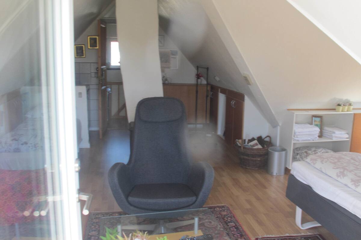 Ein Schlafzimmer mit Bett, Stuhl, Kleiderschrank und einem kleinen Tisch mit Lampe.