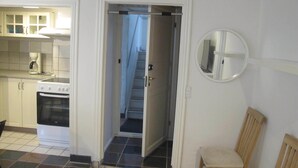A kitchen with white cabinets, a stove, and a coffee maker. There is a wooden chair and a mirror on the wall. - Guesthouse Sharon Aarhus (Aarhus)