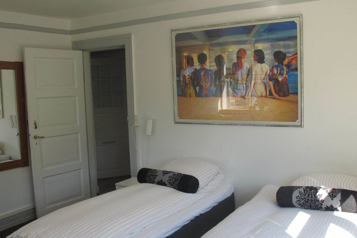 Ein Hotelzimmer mit zwei Betten, einem Bild an der Wand, einer Tür und einem kleinen Tisch.