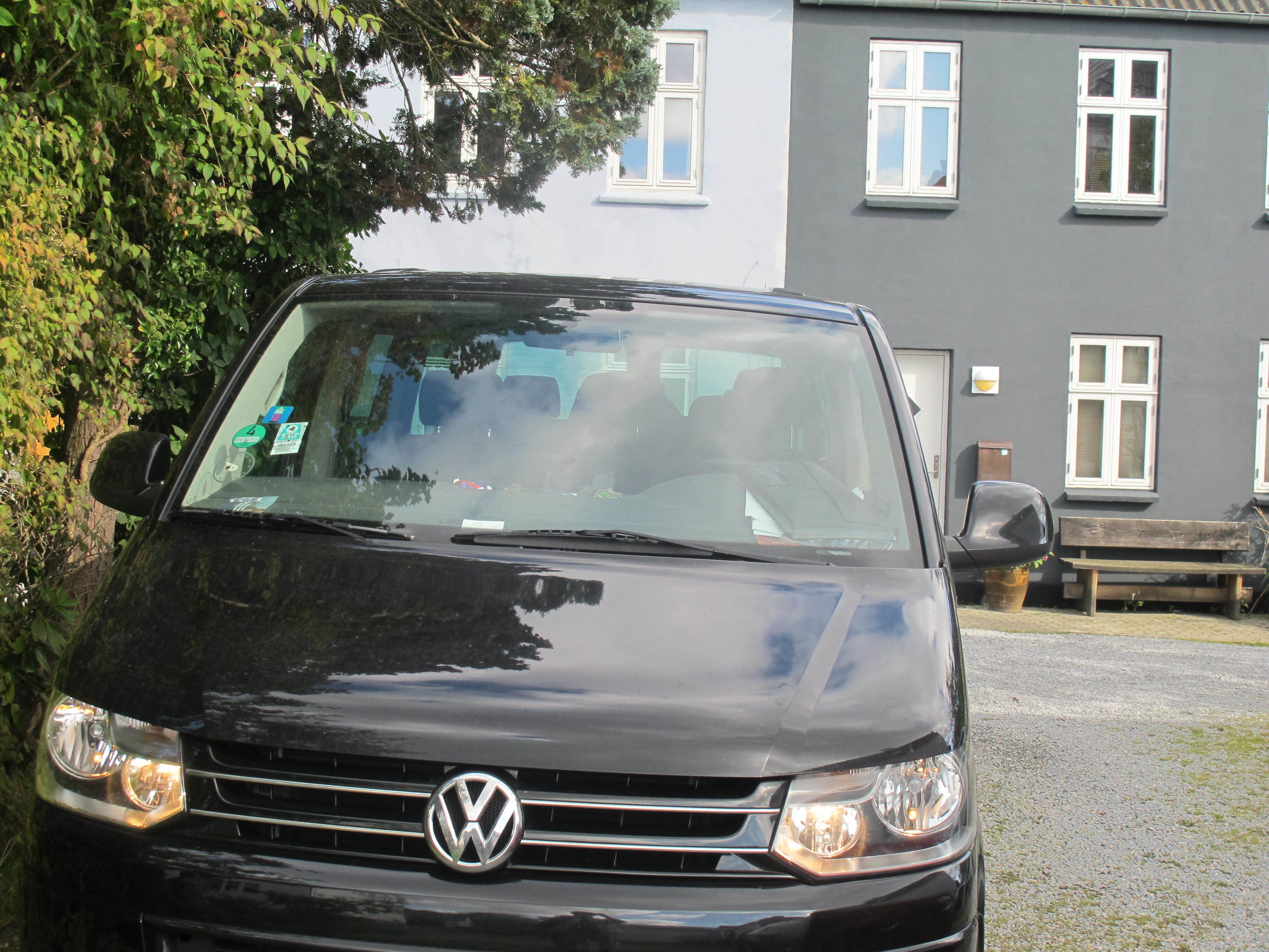 Une voiture Volkswagen noire est garée devant un immeuble doté de nombreuses fenêtres et d’un banc.
