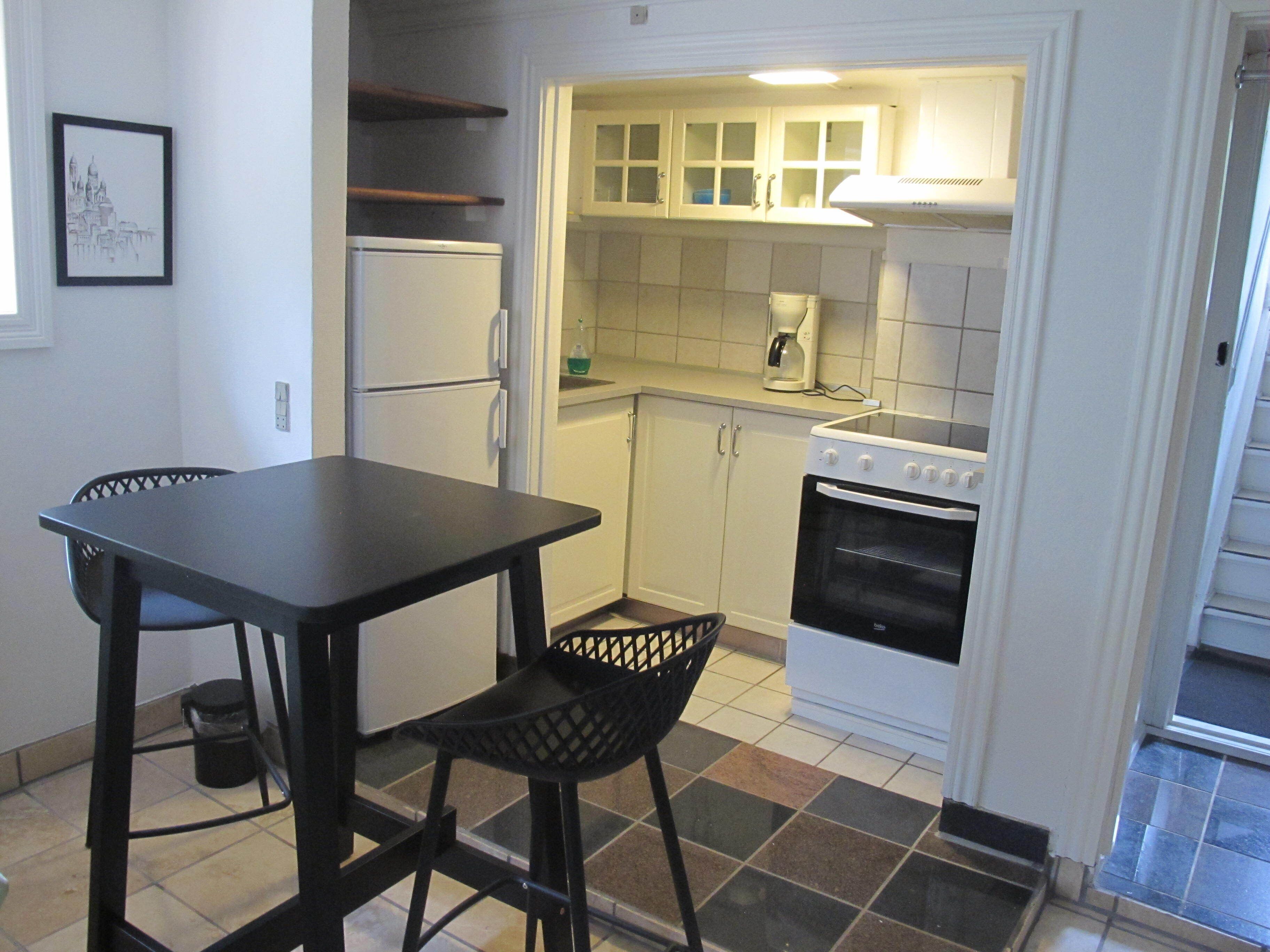 Una cocina compacta con mesa, sillas, refrigerador, estufa y armarios.