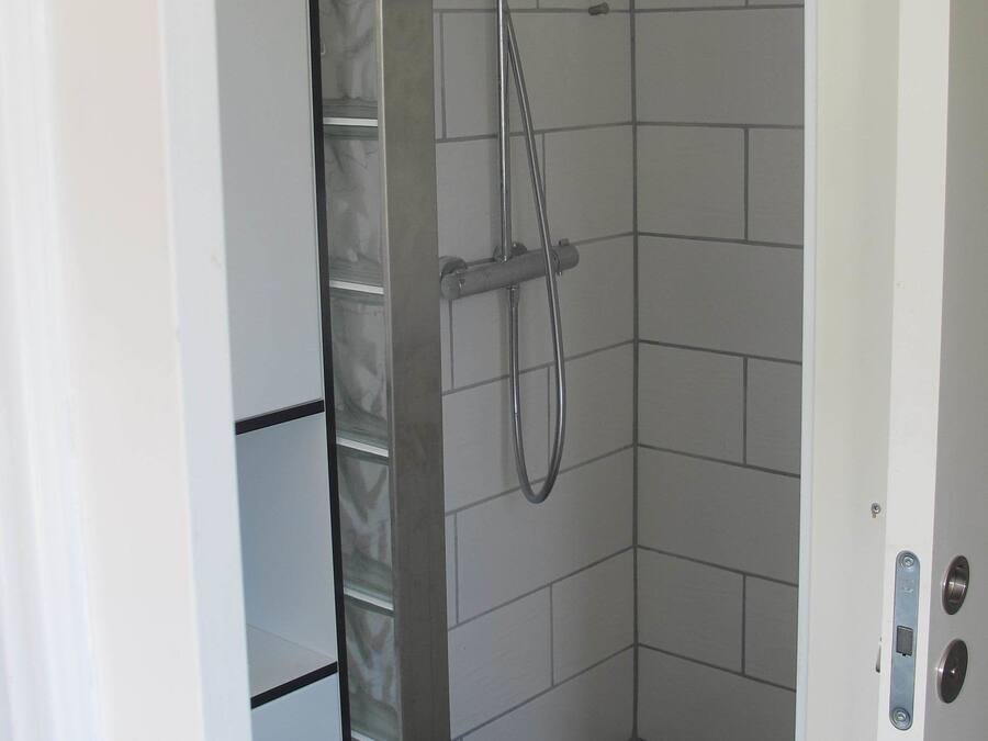 Ducha con cabezal de ducha de mano y cabezal empotrado en la pared, paredes con azulejos y una puerta con manija.