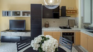 A modern kitchen with a TV, dining table, and a decorative white flower arrangement. - Chez Mamie Flat (Salerno)
