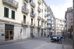 A street with parked motorcycles, a building with closed shutters, and a flag on a balcony.