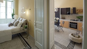 A modern bedroom with a bed, bedside table, lamp, and a view of the kitchen. - Chez Mamie Flat (Salerno)