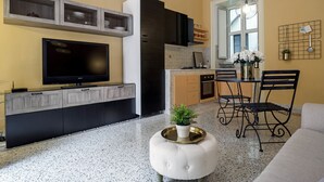A modern kitchen with a TV, cabinets, and a dining area with a table and chairs. - Chez Mamie Flat (Salerno)