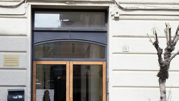 A building entrance with a glass door, a small tree, and a number sign '70' on the wall. - Chez Mamie Flat (Salerno)