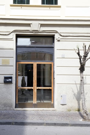 A building entrance with a glass door, a small tree, and a number sign '70' on the wall. - Chez Mamie Flat (Salerno)