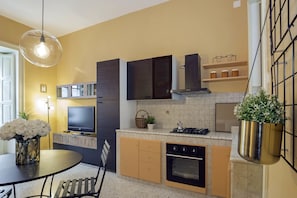 A modern kitchen with a dining area, a TV, and a hanging plant.