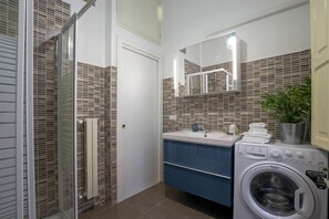 A modern bathroom with a glass shower enclosure, a built-in sink with a mirror, and a front-loading washing machine.