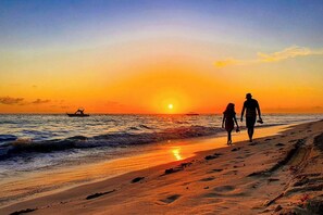 A sunset over a beach with two people walking along the shore.