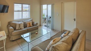 A living room with a sofa, a glass coffee table, and a TV mounted on the wall. - The Nook, Langebaan 4-Sleeper (Langebaan)