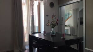 Een eetgedeelte met een donker houten tafel, zwarte stoelen, een vaas met bloemen en een hanglamp.