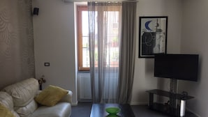 Een woonkamer met een bank, een salontafel, een televisie en een raam met gordijnen.
