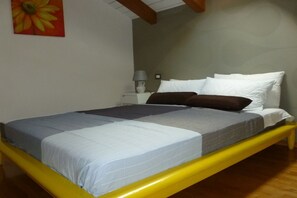 Una cama con estructura amarilla, ropa de cama blanca y una lámpara sobre la mesita de noche.